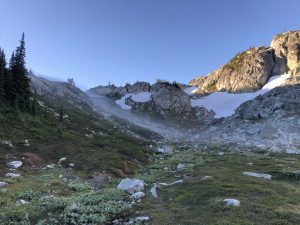 early morning sun softly lights a mountain ridge as a ribbon of low lying fog rolls into the valley