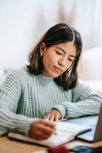 young woman thoughtfully writing in gratitude journal